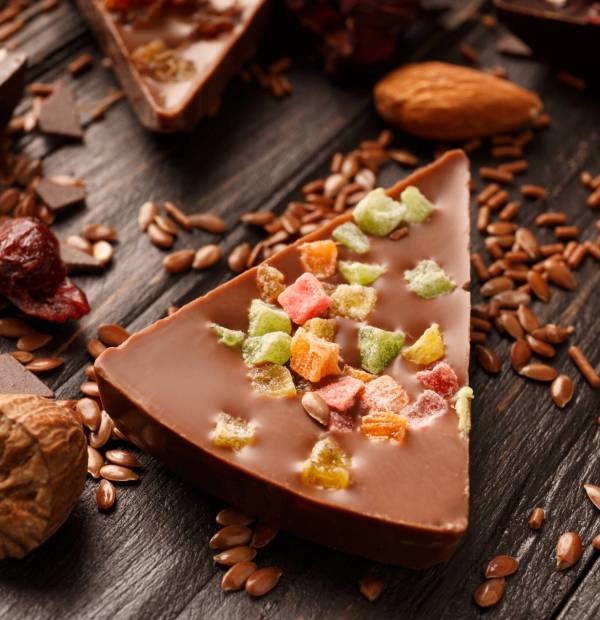 Creative composition chocolate in the shape of a pizza with candied fruits, nuts, dry berries, chocolate pizza and ingredients on a dark wooden background.